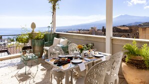 Una terraza con mesa lista para comer, plantas en macetas y vista al mar y las montañas.