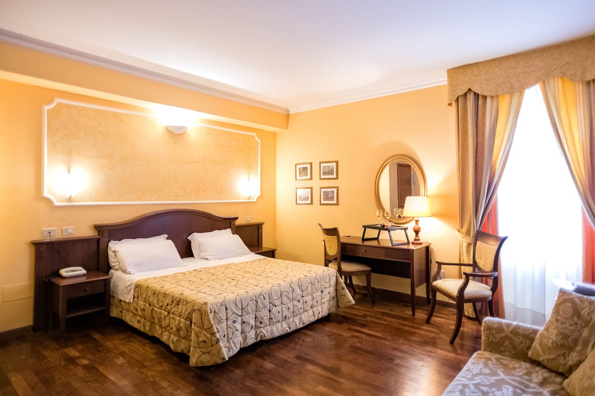 Une chambre d’hôtel avec un grand lit, un bureau avec une chaise, une table de chevet et un miroir.