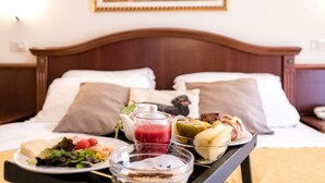 A neatly made bed with a wooden headboard, a bedside table with a tray of breakfast items, and a framed picture on the wall. - Grand Hotel Italia (Orvieto)