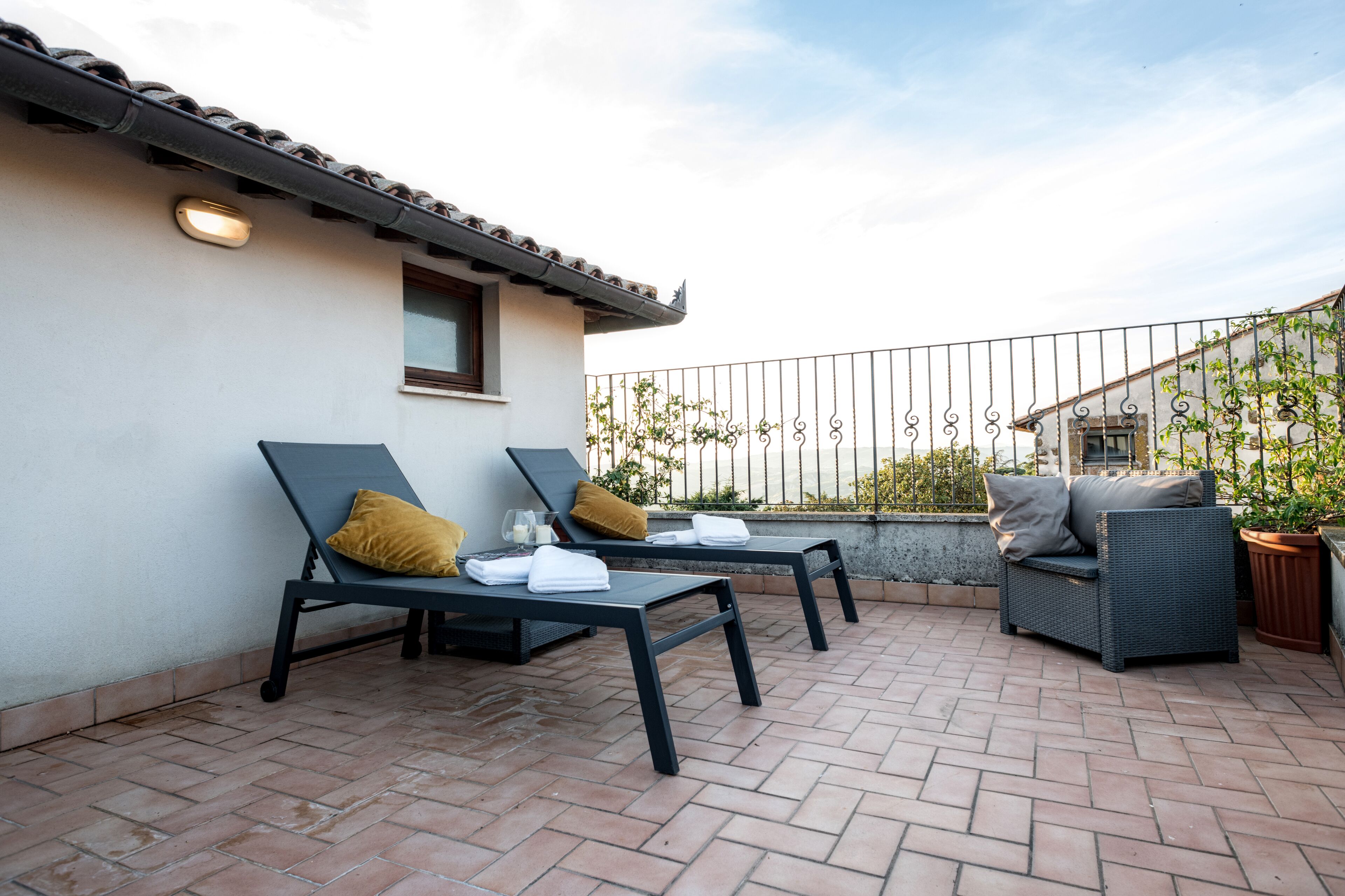 A rooftop patio with two lounge chairs, a wicker sofa, and a potted plant.