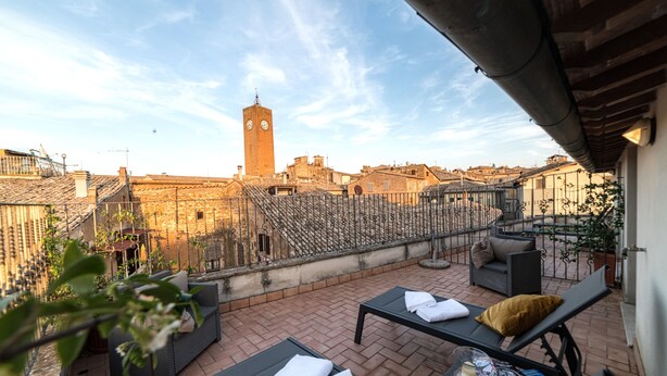 A rooftop terrace with outdoor seating, a view of a clock tower, and a cityscape in the background. - Grand Hotel Italia (Orvieto)