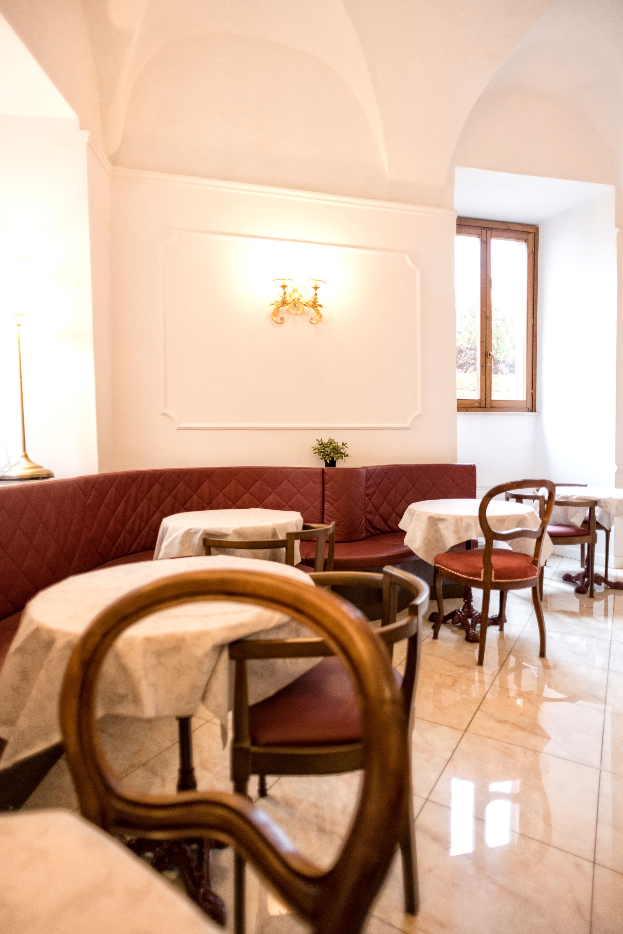 Ein Restaurant mit einer roten gepolsterten Bank, runden Tischen und Holzsesseln.