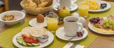 A breakfast table with croissants, bread, eggs, tomatoes, cucumbers, yogurt, juice, coffee, ham, cheese, and grapes.