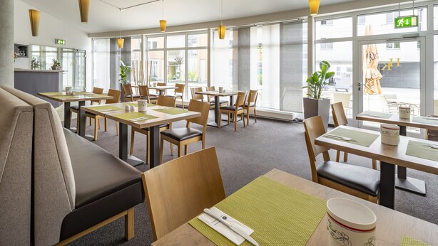 A modern dining area with multiple tables and chairs, large windows, and a central counter.