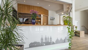 A reception area with a modern design, featuring a reception desk, a large vase with flowers, and a cityscape mural on the wall.