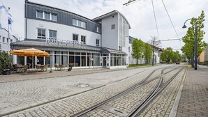 A modern hotel with a glass facade, outdoor seating, and a tram line.