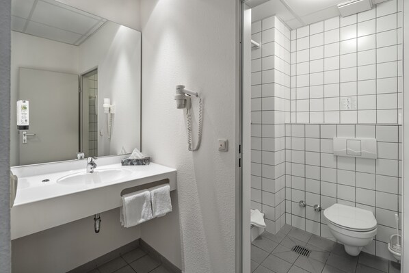 Un baño moderno con lavamanos, espejo y retrete blancos.