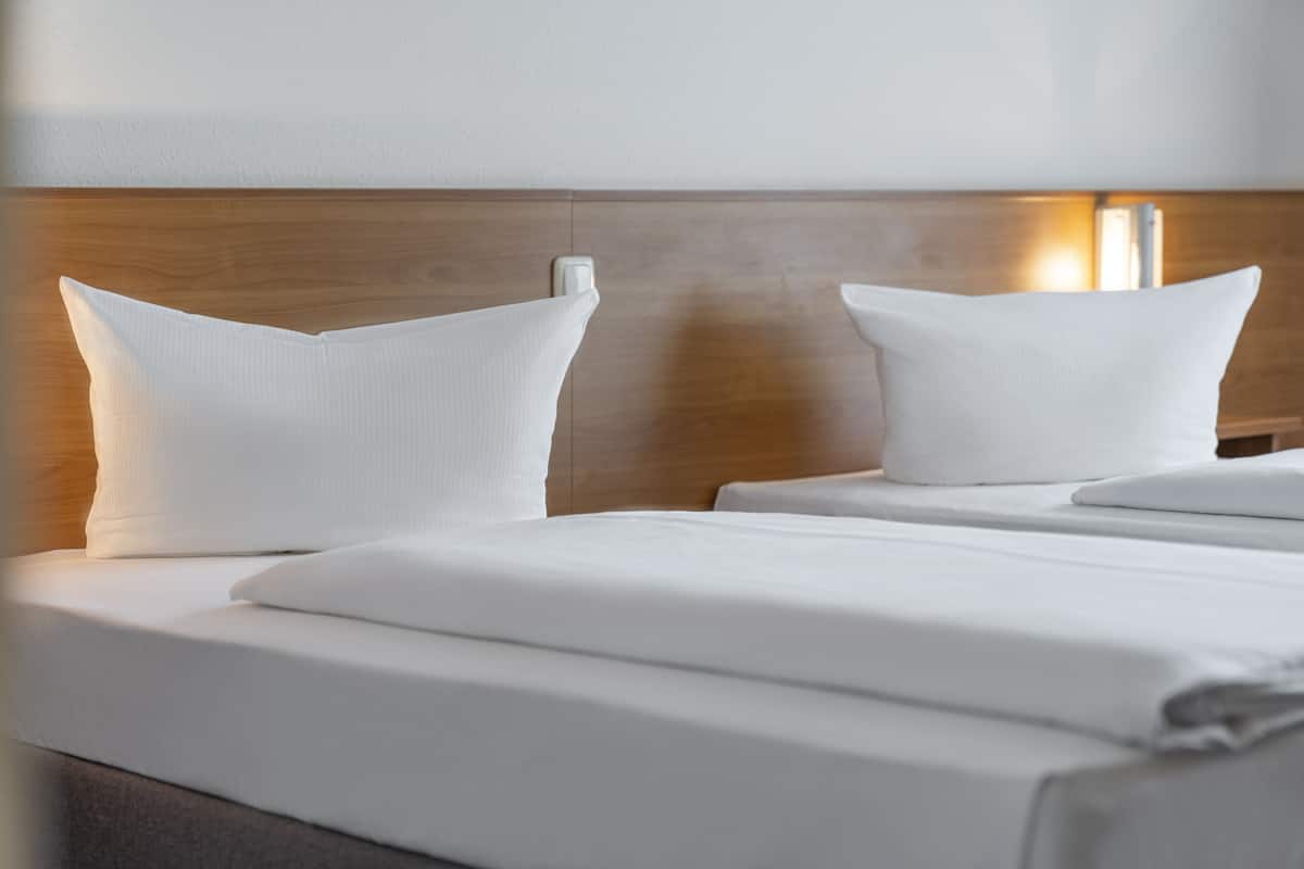 A hotel room with a wooden headboard, two white pillows, and a neatly made bed.