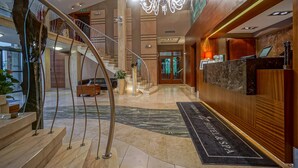 Een hotel lobby met een marmeren receptiebalie, een kroonluchter, een trap en een receptiegedeelte met een bord waarop staat 