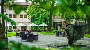 Een terras buiten met stenen vloer, zitplaatsen, parasols en een waterpartij.