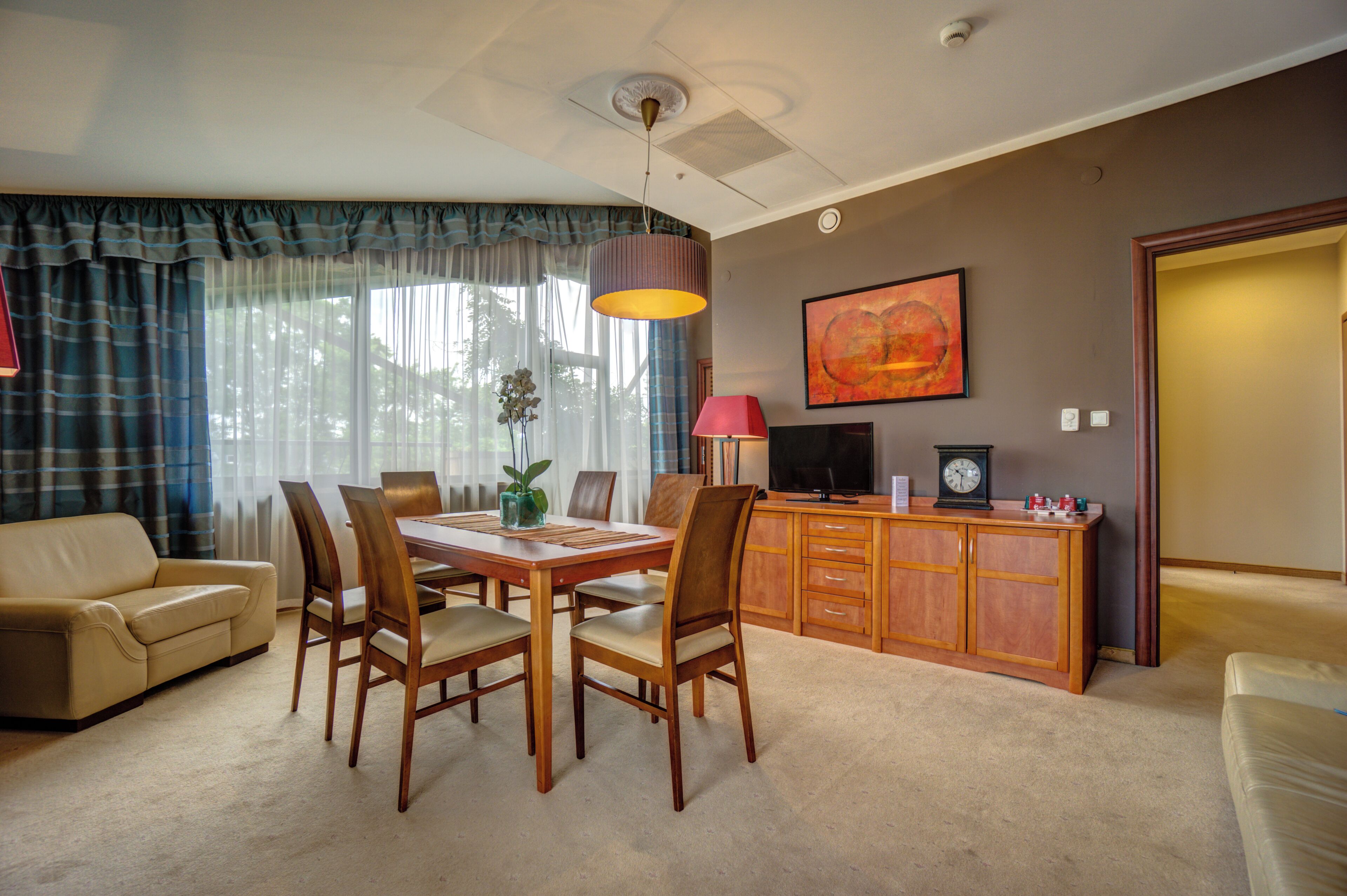 A dining area with a table, chairs, a television, and a clock on a wooden cabinet.