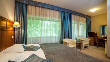 Een hotelkamer met een bed, een bureau, een stoel, een televisie en gordijnen.