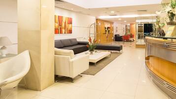 Un moderno vestíbulo de hotel con una recepción, un sofá negro, un sillón blanco y una mesa de centro.
