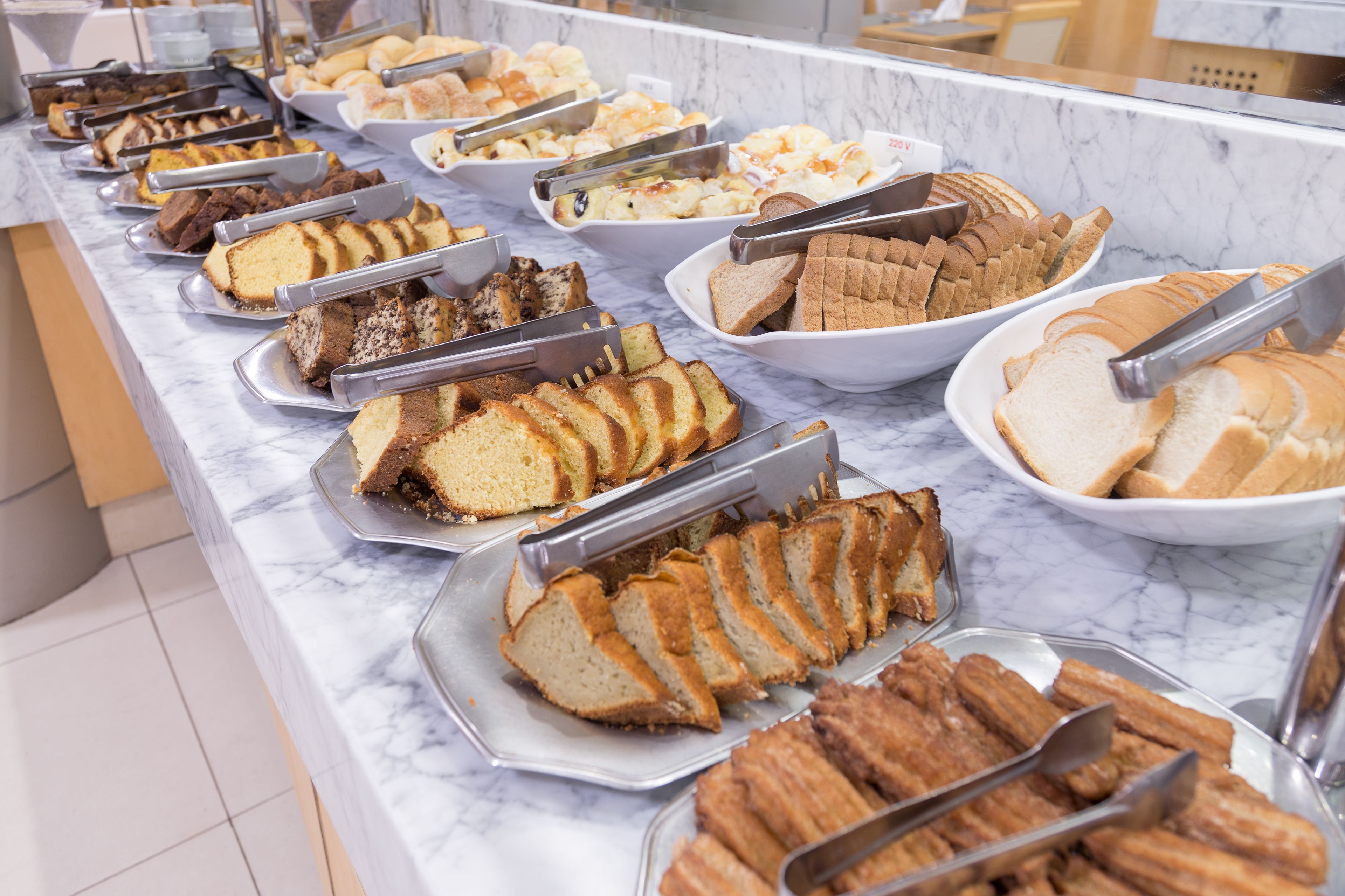 A buffet with various sliced breads and pastries on trays.