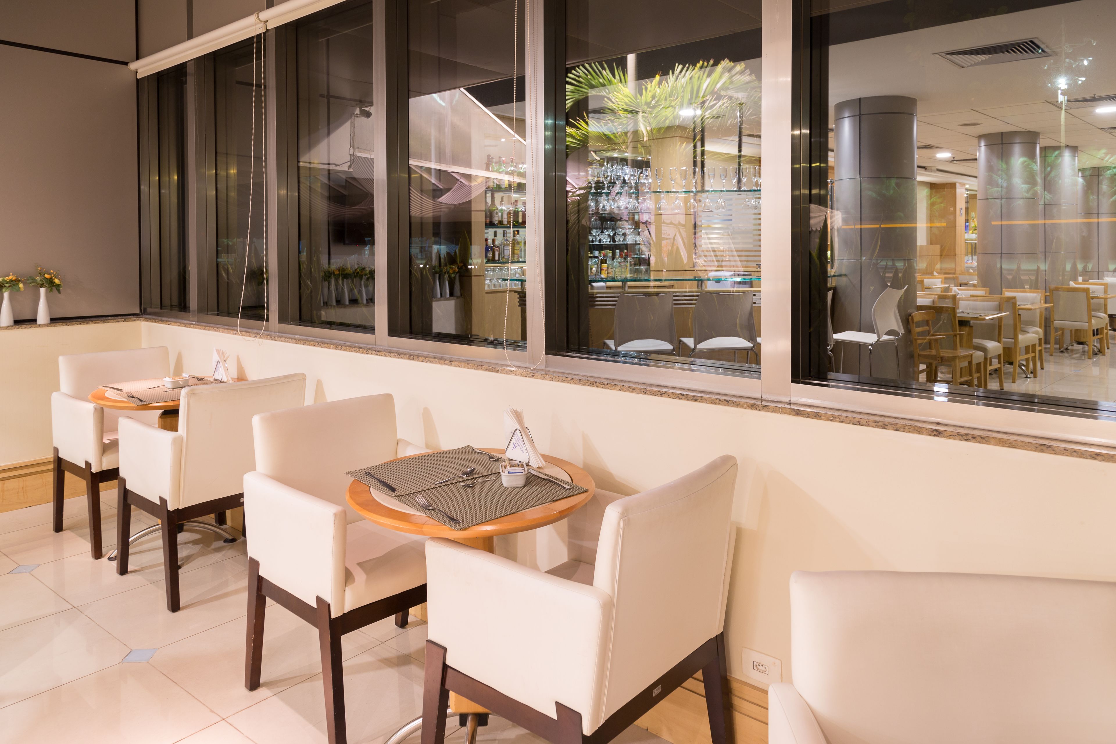 Un restaurante con una decoración moderna, que presenta una larga barra con sillas y mesas, ventanas amplias y vistas al área exterior.