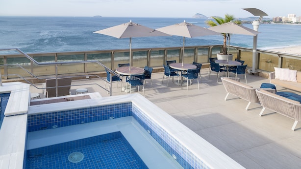 Un área de piscina en la azotea con vistas al océano, mobiliario exterior y sombrillas.