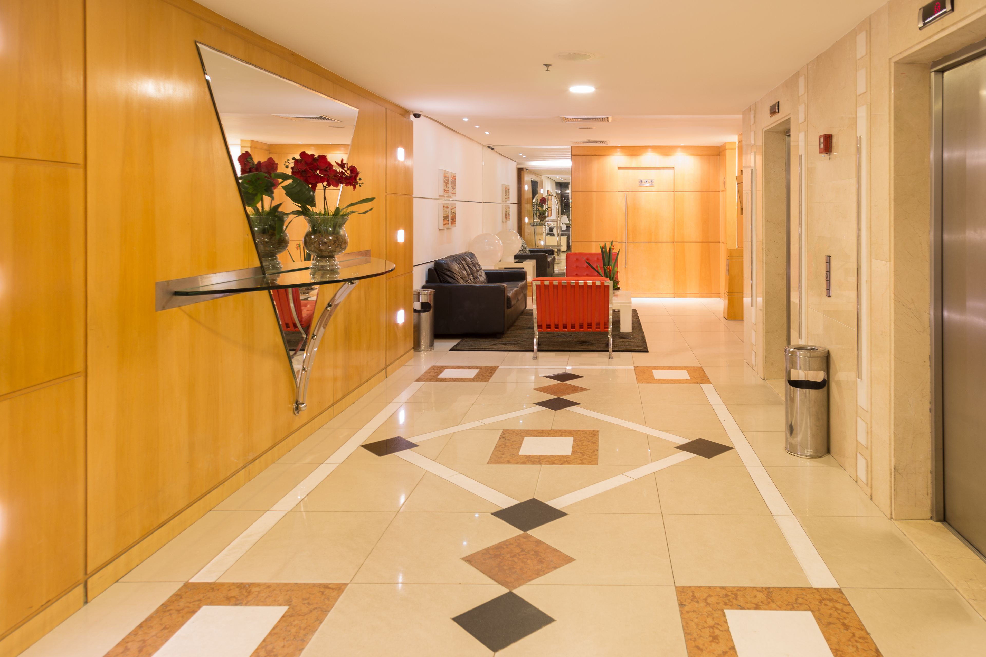 A modern hotel lobby with a glass coffee table, a sofa, and a red accent wall.