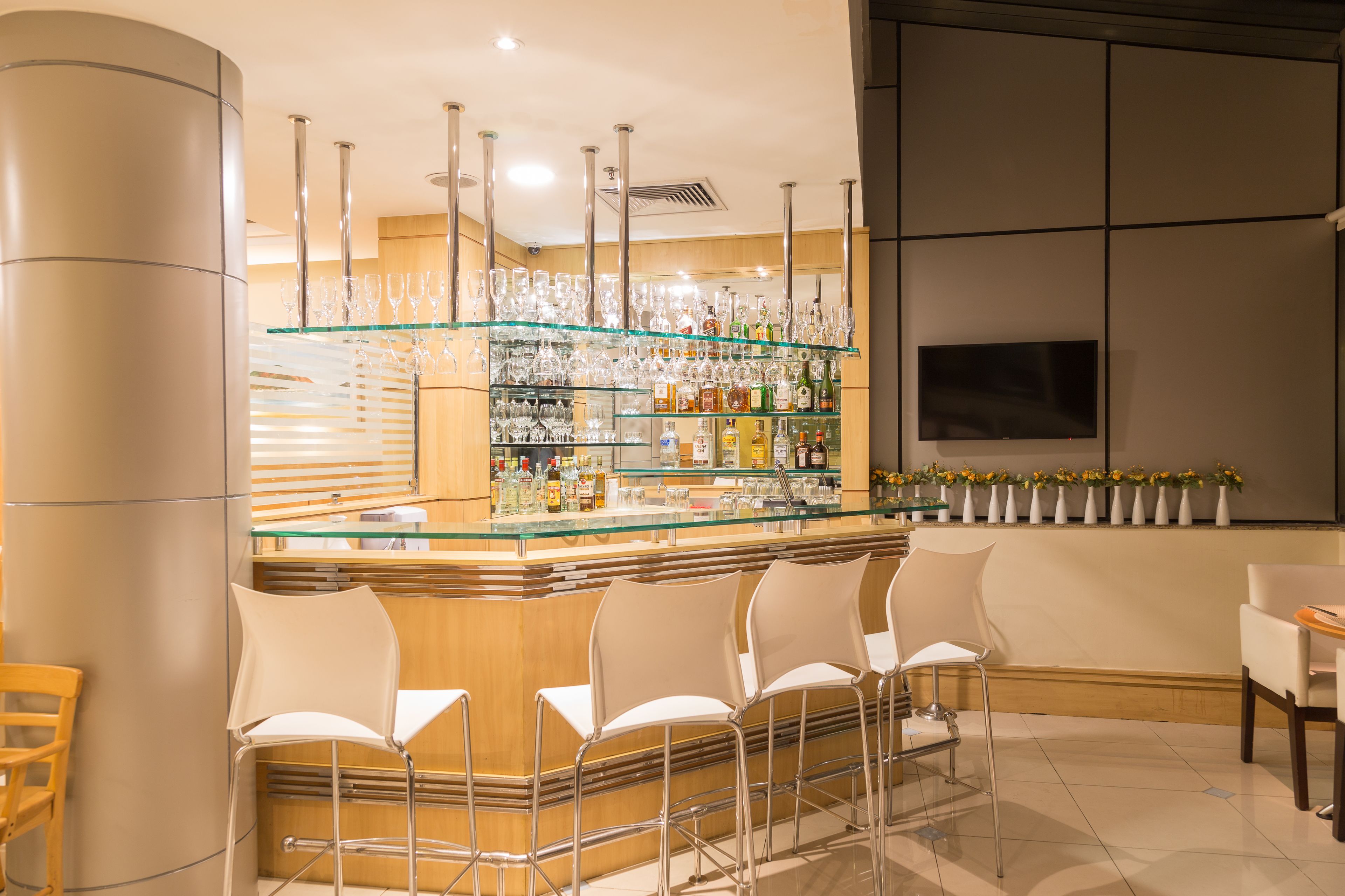 A bar area with a glass display shelf, bar stools, and a variety of bottles.