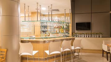 A bar area with a glass display shelf, bar stools, and a variety of bottles.