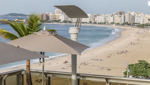 Vista a la playa desde un balcón con una planta en maceta y una sombrilla.