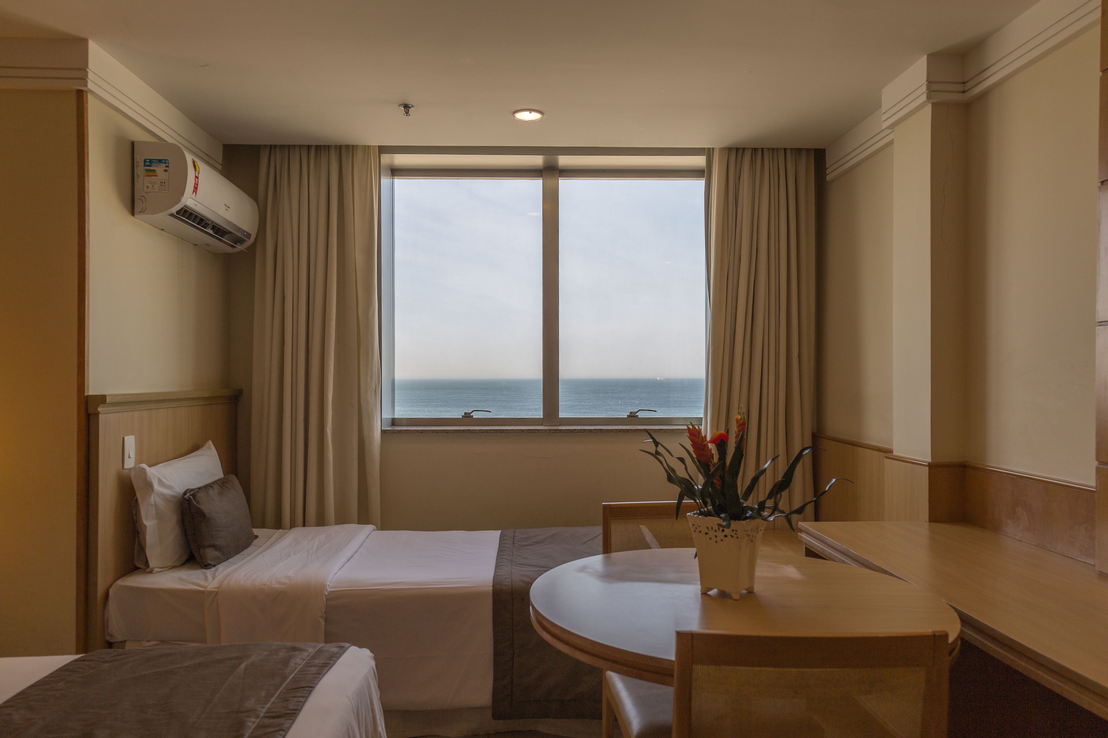 Habitación de hotel con dos camas, una mesa de comedor y vista al mar.
