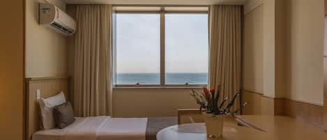Habitación de hotel con dos camas, una mesa de comedor y vista al mar.