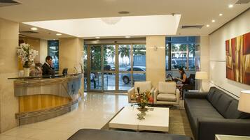 A hotel lobby with a reception desk, seating area, and large windows.