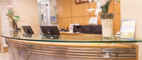 A reception desk with glass top, a clock, and a vase of white flowers.