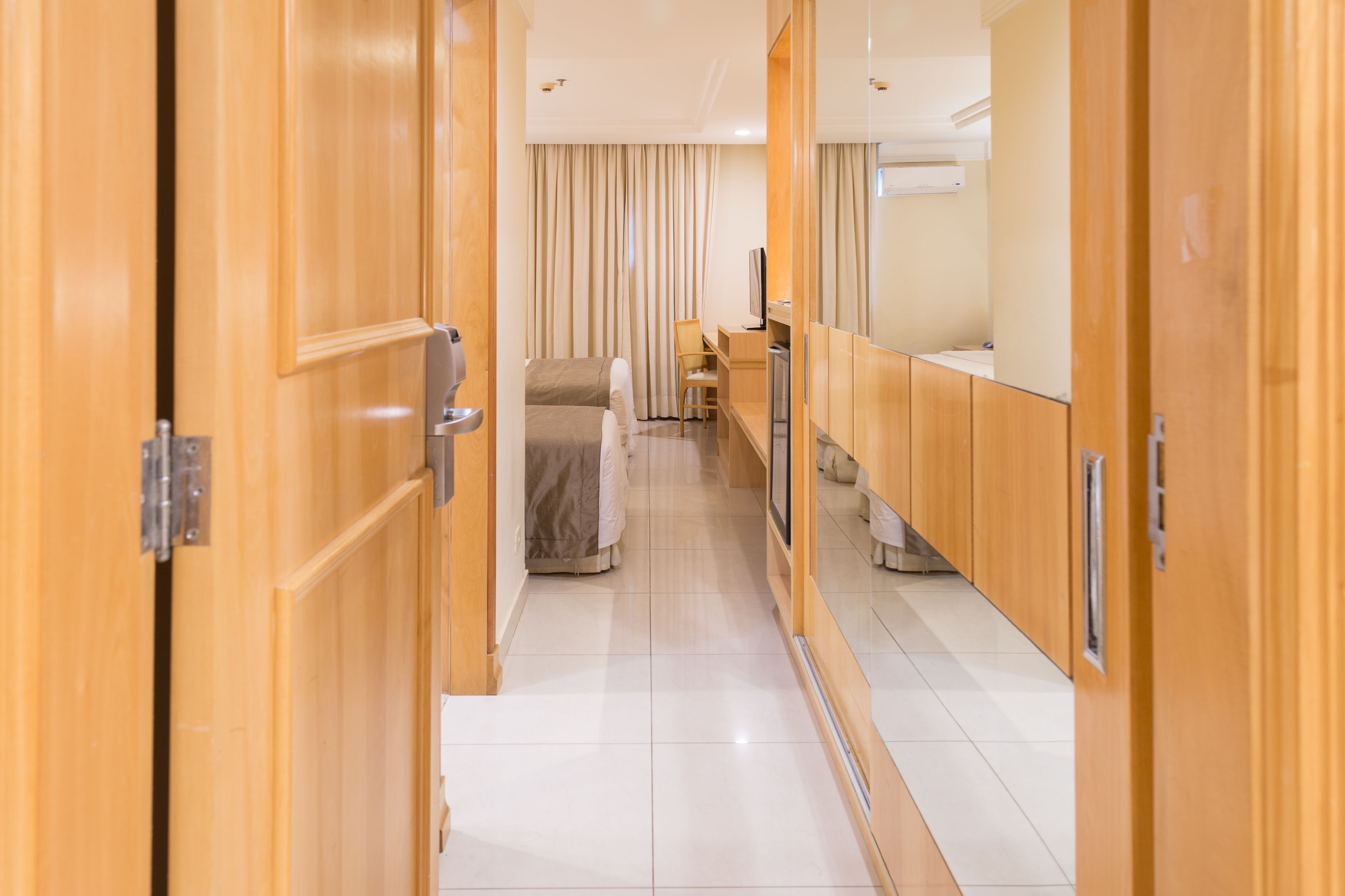 A hotel corridor with wooden doors, a bed, a desk, and a television.