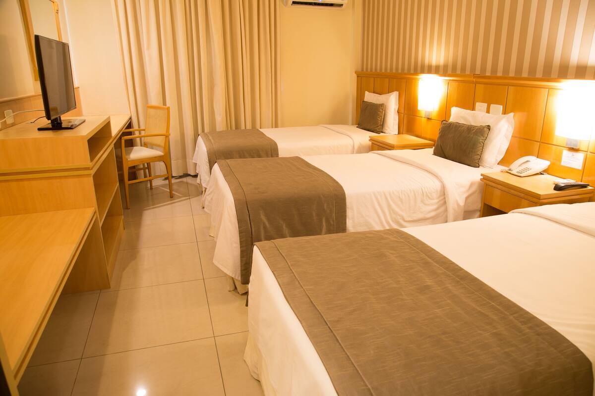 A hotel room with two beds, a desk with a computer, a chair, and a bedside table with a phone and remote control.