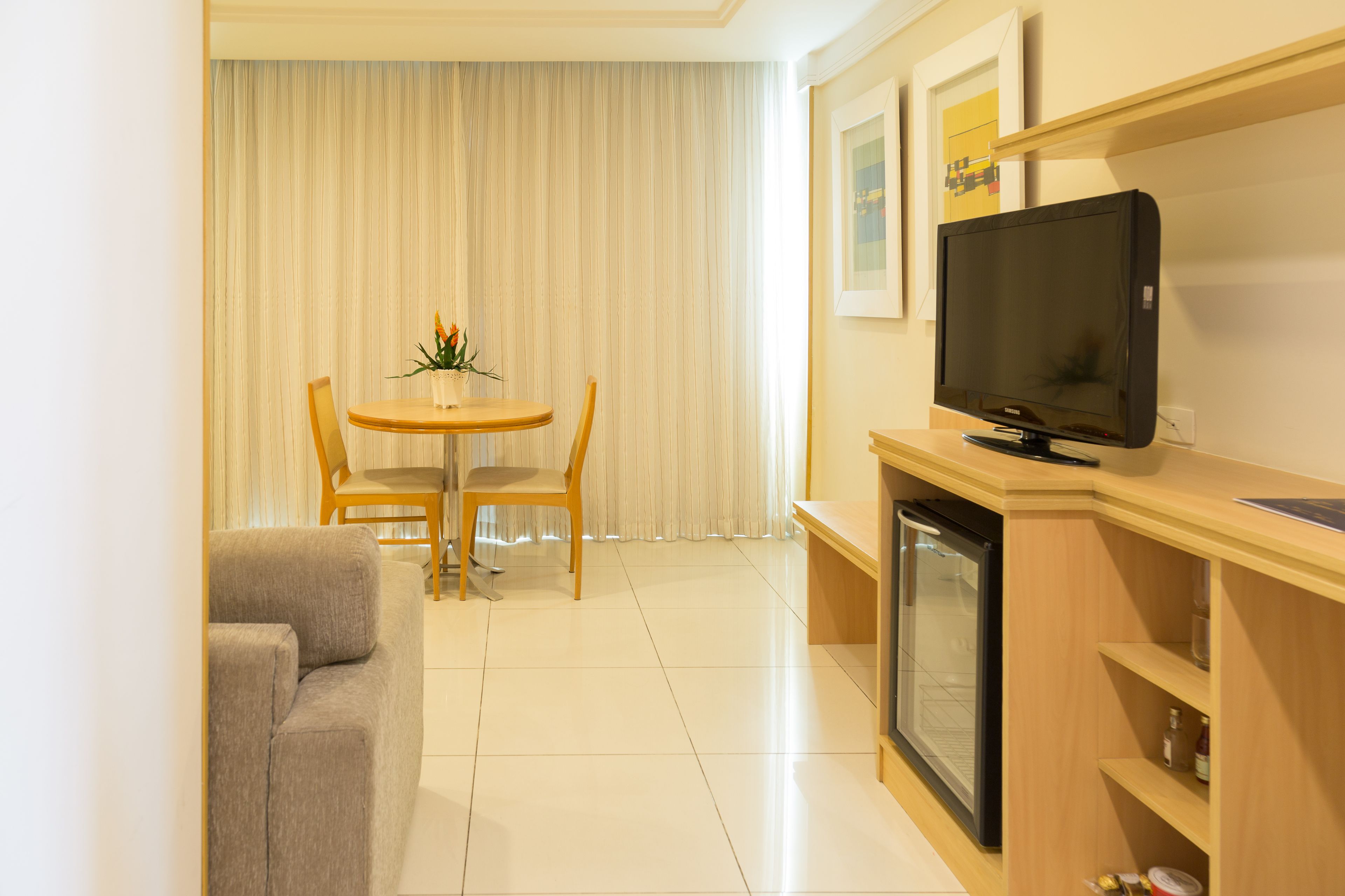 A modern living room with a sofa, a dining table with chairs, a television, and a mini-fridge.