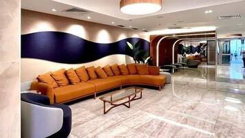 A modern lobby with a curved orange sofa, a coffee table, and a large wall with a wave-like design.