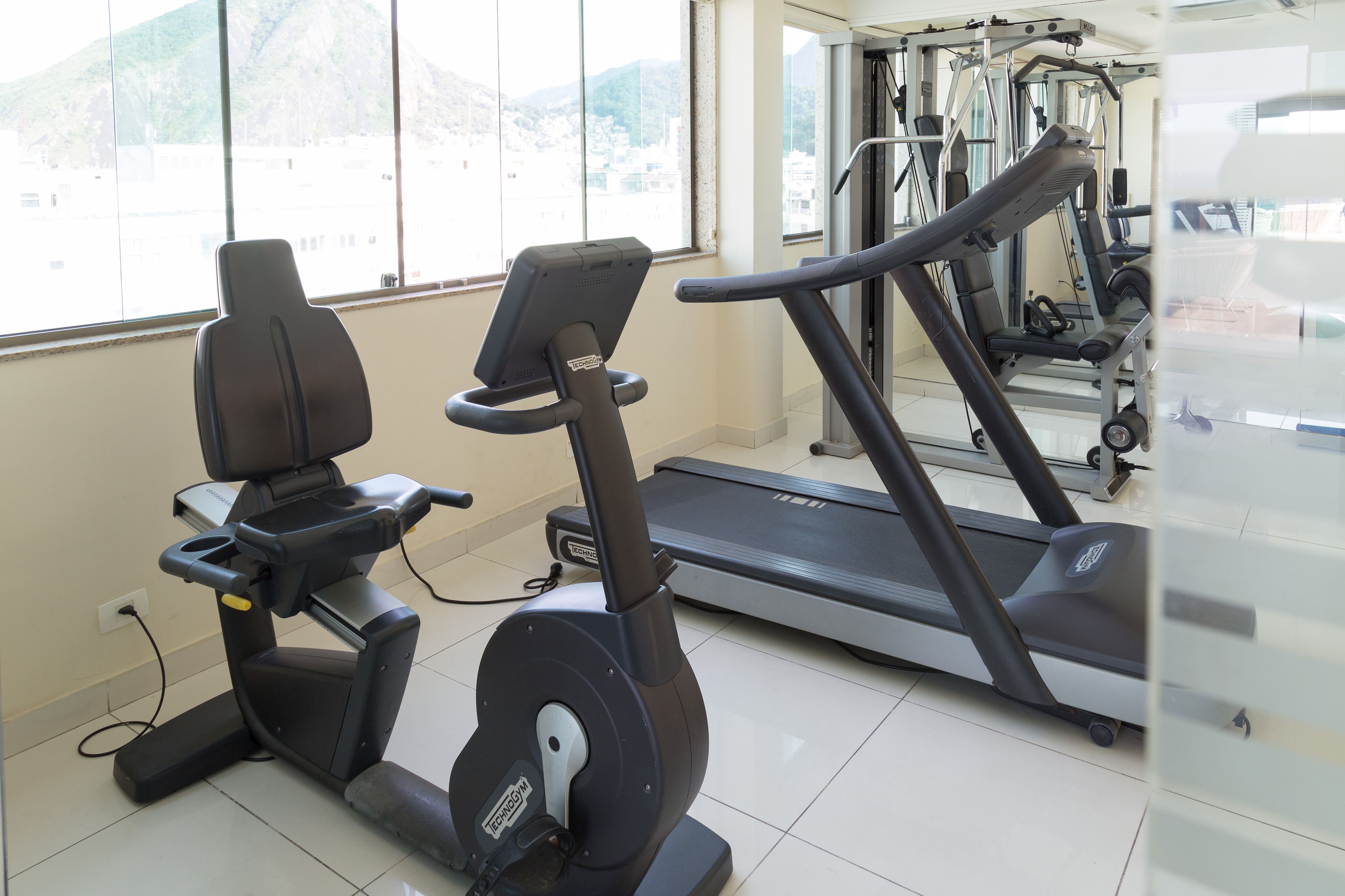 Une salle de sport équipée de matériel d’exercice, notamment un vélo d’appartement et un tapis de course, et dotée de grandes fenêtres offrant une vue sur l’extérieur.