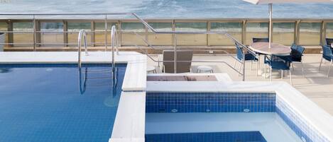 Una piscina con vista al océano, una playa y una mesa con sillas.