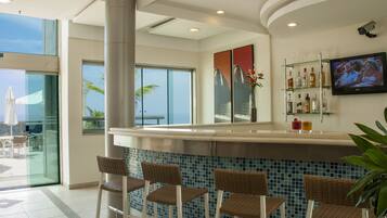 Zona de bar con mostrador, taburetes, televisor y vistas al exterior.