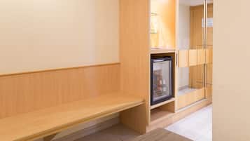 A modern hotel room with a wooden bench, a minibar, and a wardrobe with mirrors.