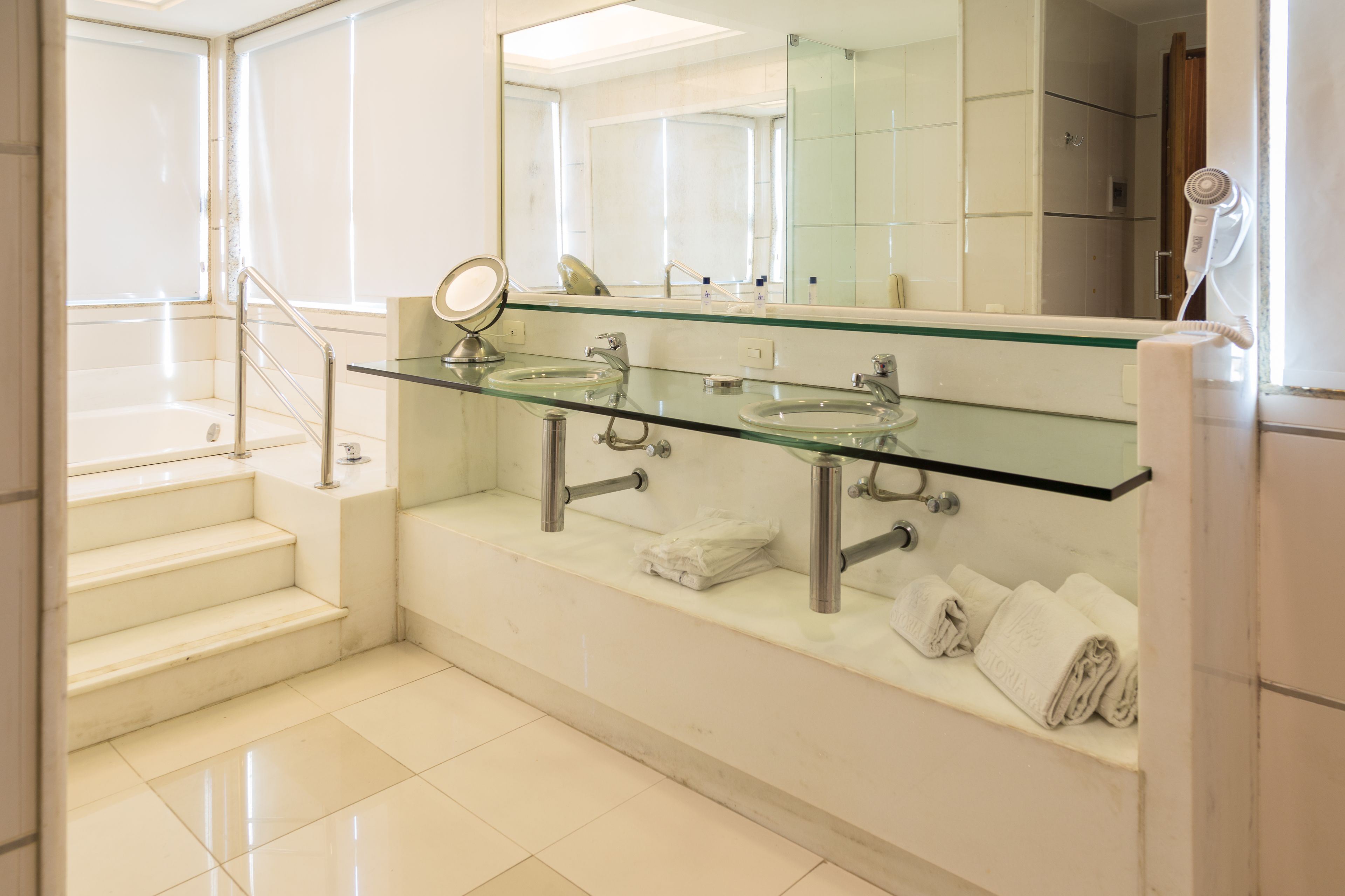 A modern bathroom with two glass sinks, a large mirror, and a towel rack.