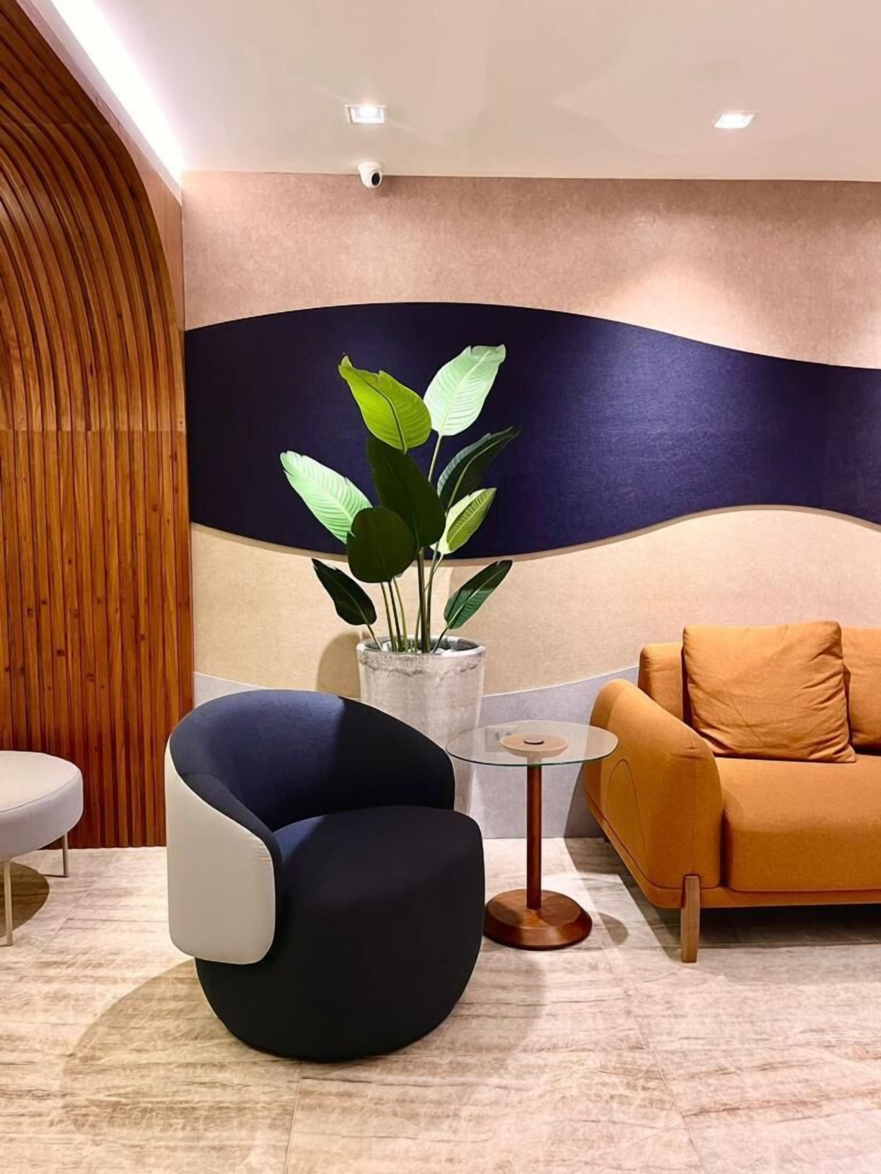 A modern interior with a round table, a blue chair, a sofa, and a potted plant.