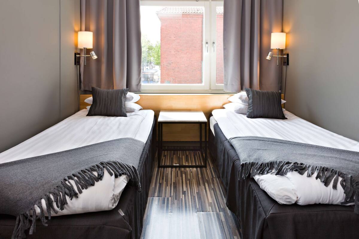 Une chambre d’hôtel avec deux lits simples, une petite table et deux lampes fixées au mur.