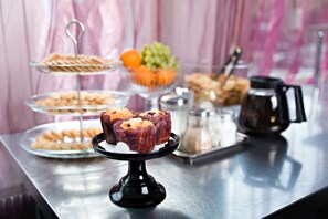 Een buffettafel met diverse etenswaren, waaronder gebak en fruit, en een koffiezetapparaat.