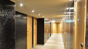 Een hotelgang met spiegelende wanden, houten deuren en een kamerbreed tapijt met patroon.