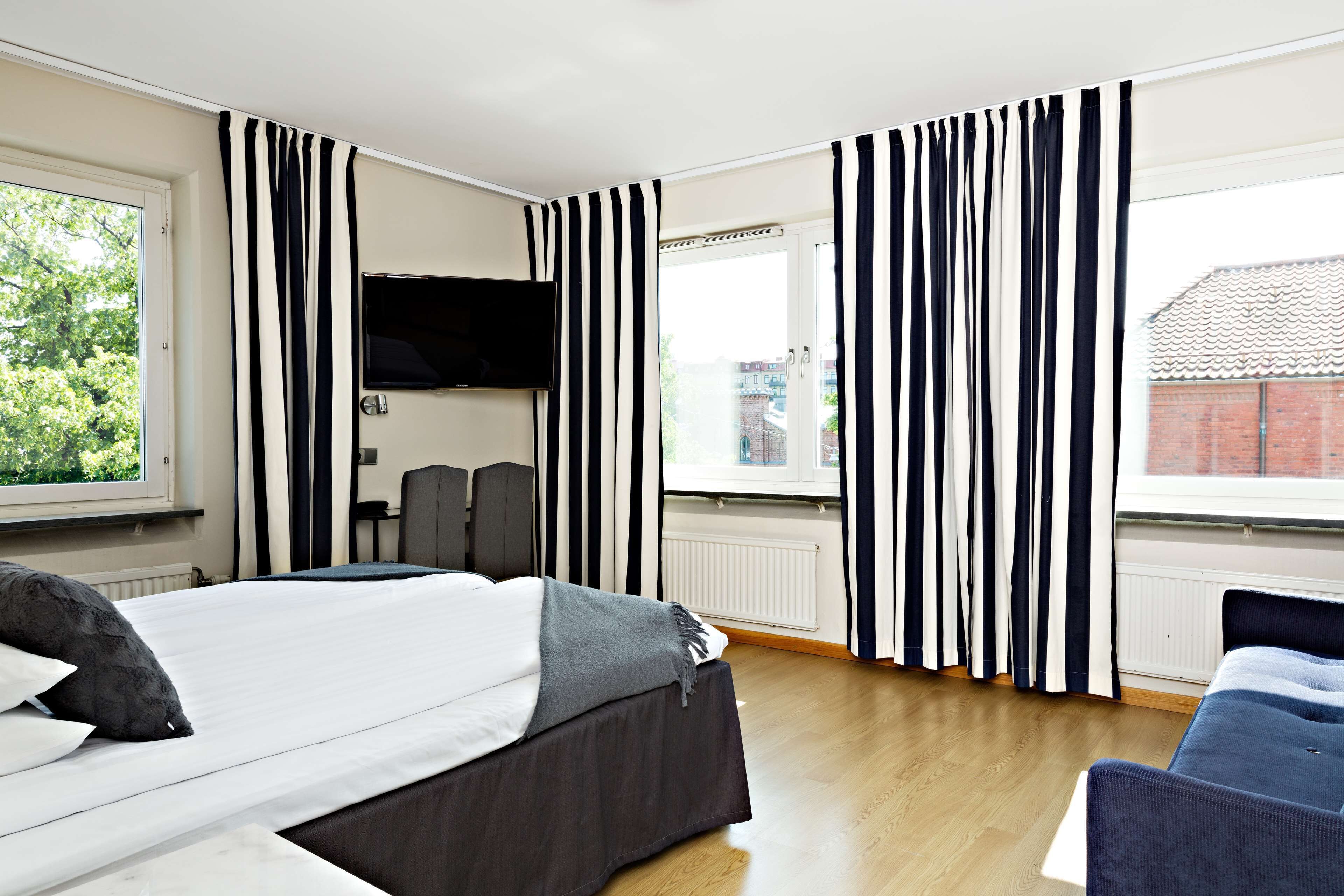 Ein Hotelzimmer mit einem Bett, einem an der Wand befestigten Fernseher, einem Schreibtisch und einem Stuhl.