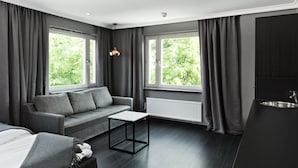 Een moderne hotelkamer met een grijze bank, een kleine tafel, een bed en een kitchenette met een spoelbak.