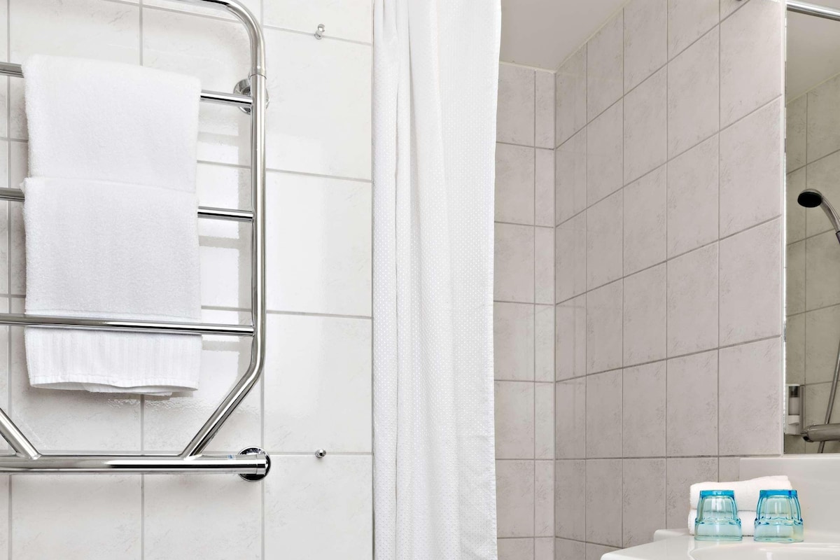Une salle de bain avec une baignoire blanche, un rideau de douche, un porte-serviettes avec des serviettes et un lavabo avec deux bouteilles d’eau.