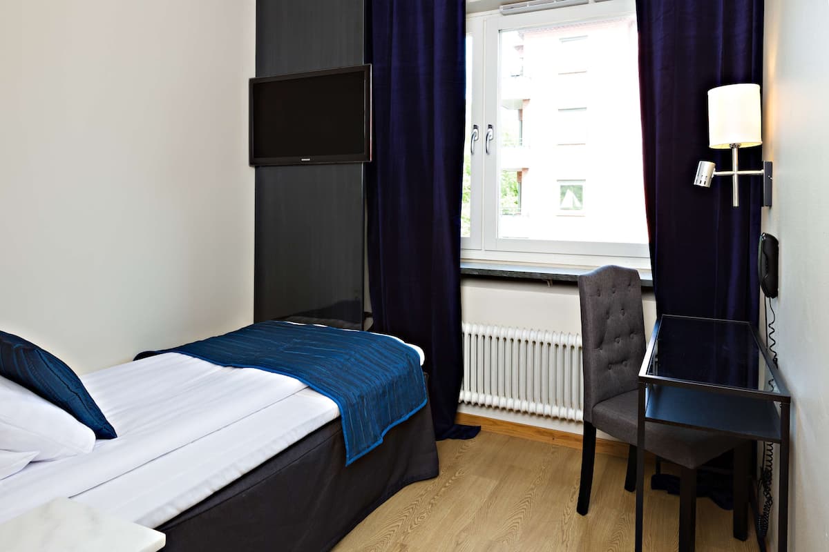 Une chambre d’hôtel avec un lit, un bureau, une chaise, une télévision et une fenêtre avec des rideaux.
