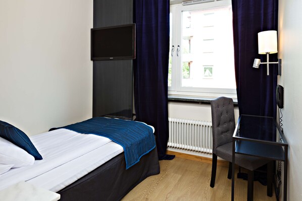 Ein Hotelzimmer mit Bett, Schreibtisch, Stuhl, Fernseher und einem Fenster mit Vorhängen.