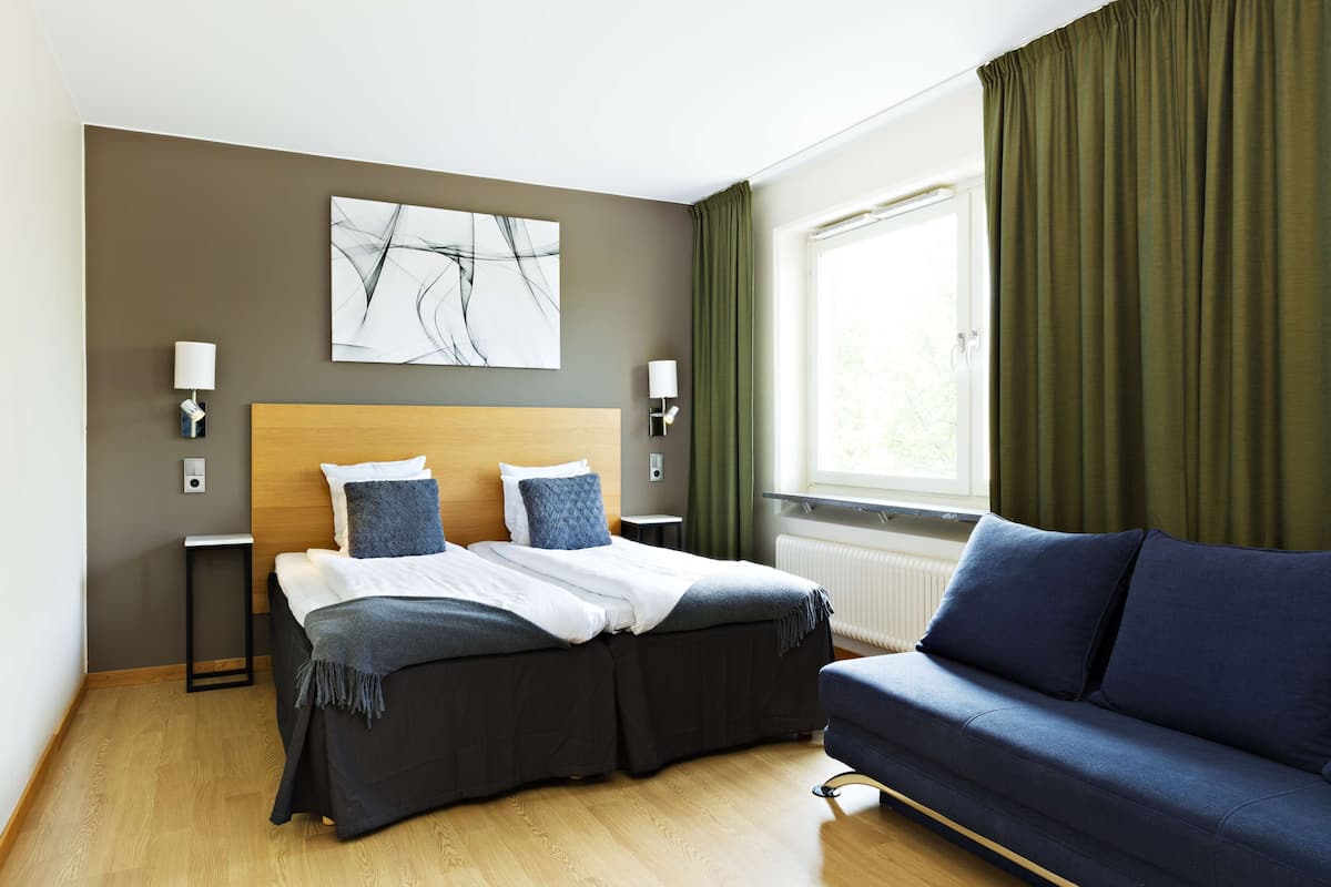 Une chambre d’hôtel moderne, équipée d’un lit, d’un canapé, d’un tableau au mur et d’une fenêtre avec des rideaux.