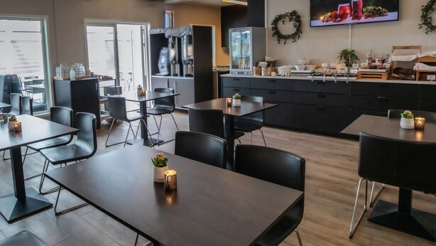 Un comedor moderno con mesas y sillas, una zona de cocina con electrodomésticos y un televisor en la pared.