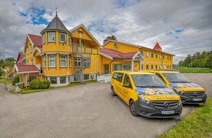 Un edificio amarillo con techo rojo, una escalera y dos furgonetas Mercedes-Benz amarillas estacionadas en la entrada.