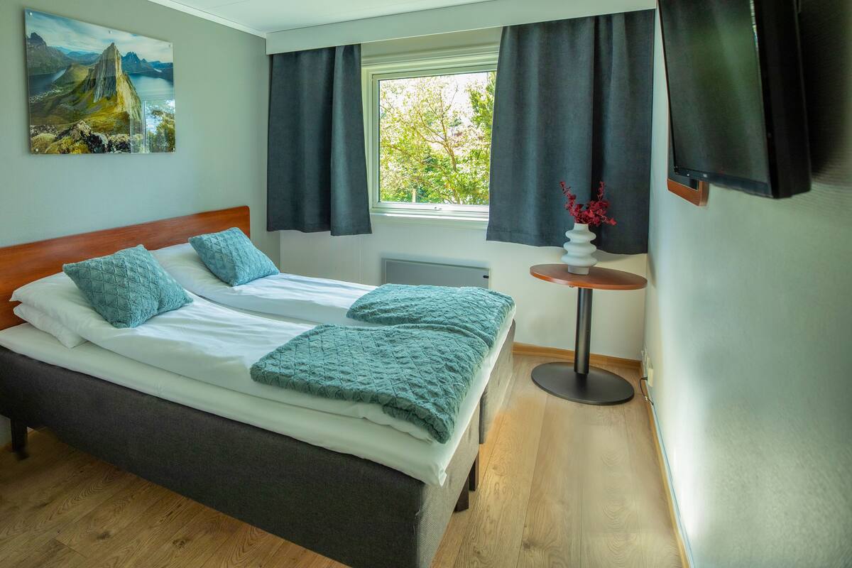 A hotel room with a large bed, a small table with a vase, and a painting on the wall.